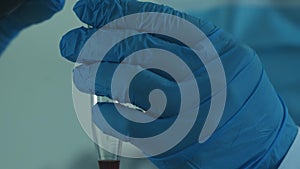 A laboratory technician in a white coat and protective gloves pours liquid into a chemical dish.