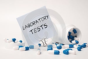 LABORATORY TESTS - inscription on paper note near blue-white pills spilling out of pill bottle. Medical concept