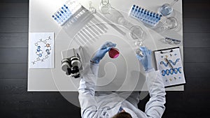 Laboratory worker examining purple liquid in flask, adding reagent, top view