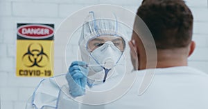 Laboratory worker in hazmat taking PCR throat sample for Covid-19 test from african american patient