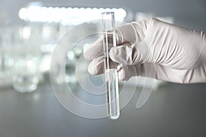 Laboratory worker holding test tube with water on blurred background