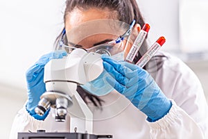 Laboratory worker looks into the microscope while holding positive and negative Covid-19 samples in her hand