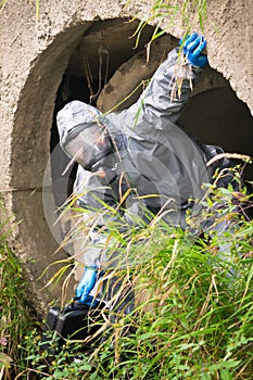 Laboratory worker in a protective suit and breathing apparatus crawls out of the pipe, side view