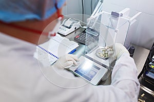 Laboratory worker in sterile rubber gloves, weighs the manufactured tablets on the control scales.