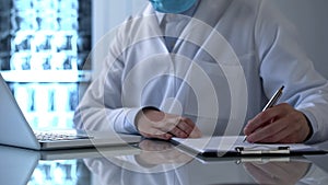 Laboratory worker typing on laptop and writing down medical observations photo