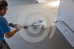 Laborer polishing sand and cement screed floor.