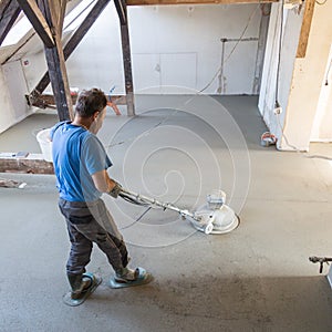 Laborer polishing sand and cement screed floor.