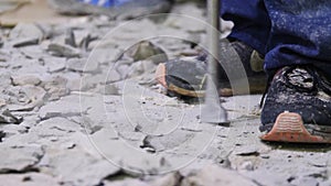 Laborer in sneakers with jackhammer breaks concrete on floor