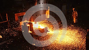 Laborer stands by tank with liquid metal and sparks spread