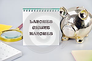 LABORES GIGUNT HANORES Translated from Latin, how Works generate honors on a white notebook on a gray background near a piggy bank