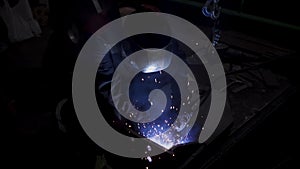 A laborious worker in a uniform and a protection mask during welding process. Clip. Welder in a workshop of a plant