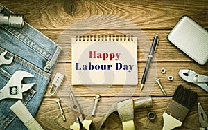 Labour day background concept - Jeans, many handy tools, notebook with happy labour day text , wooden background top view