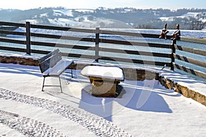 Lac view from village house. Snowy Winter rustic landscape. Wooden bench and stone table in the snow