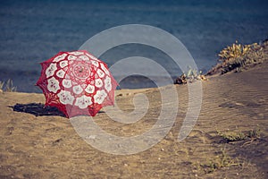 Lace fabric red umbrella on the beach on the background of the sea. Red umbrella on the sand