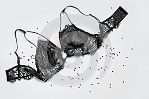 Lace sexy black womens underwear, red heart confetti on gray background flat lay top view copy space. Black lace lingerie. Fashion