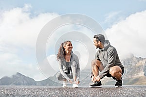 Lacing up before clocking some miles. a sporty young man and woman tying their shoelaces while exercising outdoors.