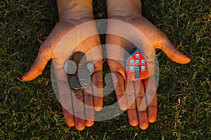 Lack of money to buy a house concept. Man holds toy house in one hand and handful of coins in another.