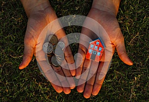 Lack of money to buy a house concept. Man holds toy house in one hand and handful of coins in another.