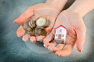 Lack of money to buy a house concept. Woman holds toy house in one hand and handful of coins in another.