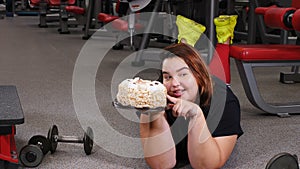 Lack of willpower. diet, fitness, healthcare. Portrait of obese young woman struggling with cake desire in gym. Sport