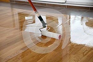 Lacquering wood floors. Worker uses a roller to coating floors