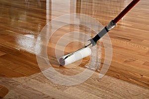 Lacquering wood floors. Worker uses a roller to coating floors