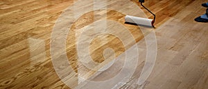 Lacquering wood floors. Worker uses a roller to coating floors