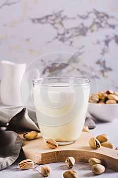 Lactose-free pistachio milk in a glass and nuts on the table vertical view