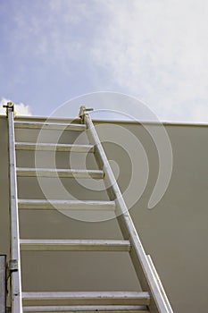 Ladder against gray color wall, blue sky background