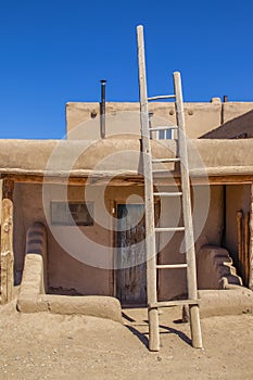 Ladder leading to second story apartments on traditional mud adobe pueblo with porch and old grunge wooden door in American