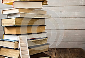Ladder on pile of old books on wooden background