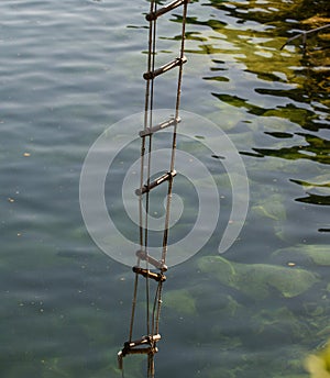 The ladder of success is never crowded at the top. Rope ladder with wooden steps. Rope over water surface. Rescue or