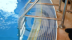 Ladder to the pool, descent to the pool. Metal staircase to the pool with blue turquoise water. Metal ladder staircase