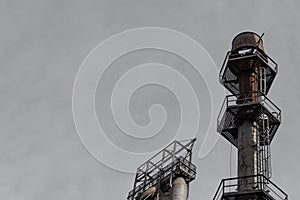 Ladders and walkways encircling an exhaust stack in an industrial complex silhouetted against gray sky, copy space