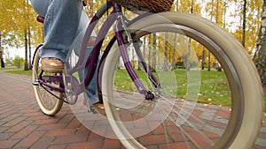 Ladies bicycle with basket in front of it in motion, female legs in ripped jeans