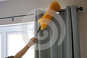 Cleaning the window and curtains area with a fluffy yellow duster