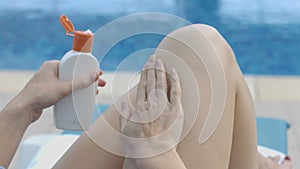 Lady applying suntan lotion on her legs with massaging movements resting by pool