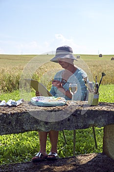 A lady artist sits in shade working on a painting