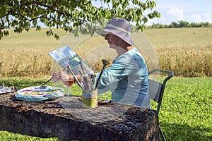 A lady artist sits in shade working on a painting