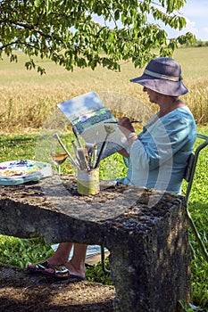 A lady artist sits in shade working on a painting