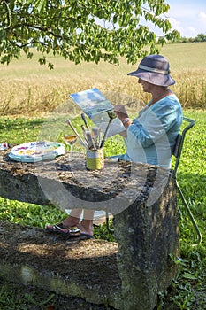 A lady artist sits in shade working on a painting