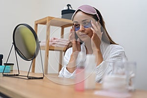 lady in a bathrobe applies eye patches, skincare routine while looking in mirror during a spa day.