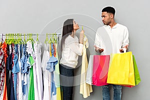 Lady begging clothes from confused man holding shopping bags.