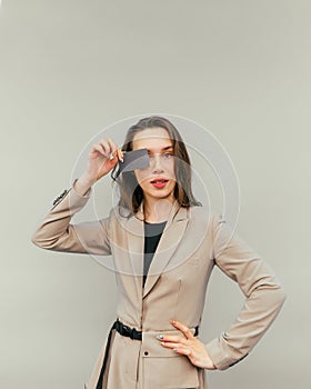 Lady in a beige suit on a beige background with a bank card in hand stands and looks at the camera with a serious face