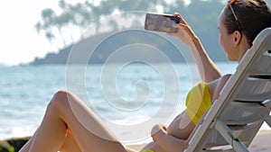 Lady in bikini makes selfie using phone while lying on sunbed