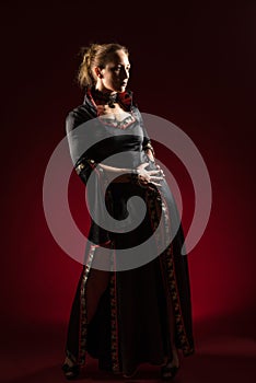 Lady in black gown standing and posing in studio. Portrait of beautiful elegant woman in evening dress.