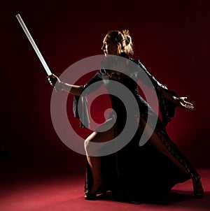 Lady in black gown with a sword standing and posing in studio. Portrait of beautiful elegant woman in evening dress.