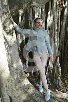 Lady in blue jacket and pink pants standing next to the trees