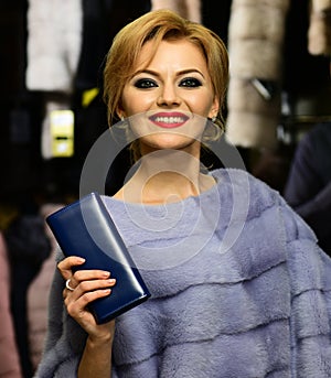 Lady with blue wallet tries expensive grey mink overcoat on