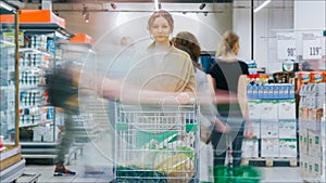 Lady in brown coat stands with shopping cart at fridges